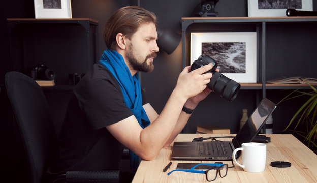 Side View Of Mature Photographer Reviewing Taken Shots In DSLR Camera Sitting At Desk At Home