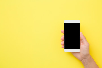 Young woman hand holding smartphone on yellow background. Empty place for text on black screen. Closeup.