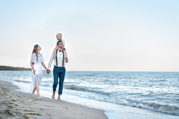 Beautiful Family walking along the sea coast. Child sits on the shoulders of the father