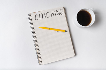 COACHING, word written on notebook. Top view of notepad, pen and cup of coffee.