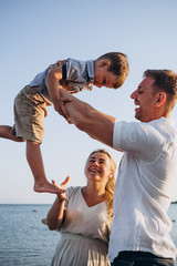 stylish man and his wife and their little son relaxing by the sea at sunset. Photo from a real...