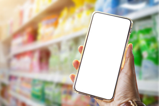 Mock up image of a woman holding and using mobile phone with blank screen at supermarket.