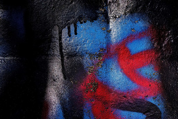 covered with black, red and blue paint with traces of vandalism, the surface of the cement wall...