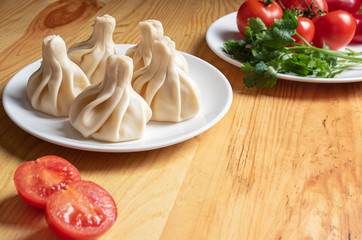 khinkali on a white plate  and fresh vegetables close-up. Dish of Georgian cuisine