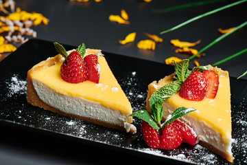 Delicious Cheesecake, decorated with strawberries on a square black plate in a dark smoky background with warm lighting. Beautiful greens on the background. Close up. Space