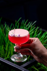 Woman holds beautiful glass with red cocktail with pink foam on the background of fresh greens