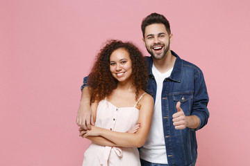 Cheerful young couple two friends european guy african american girl in casual clothes isolated on pastel pink wall background. People lifestyle concept. Mock up copy space. Hugging, showing thumb up.