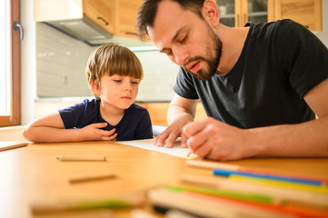 Son watching father drawing with colored pencils