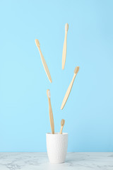 Levitation concept, flying objects. Bamboo toothbrushes fly over a white mug on a light blue background. Zero waste, no plastic. Vertical orientation.
