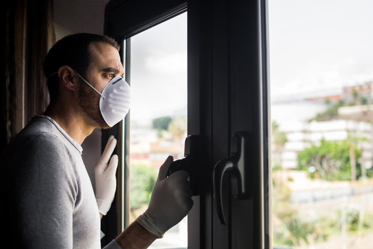 Man With Face Mask And Gloves Looking Out The Window. Stay At Home Concept.	