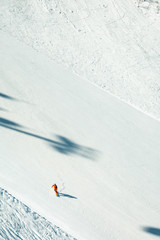 Unrecognizable snowboarder on the piste with nobody around, white snow, sunny day