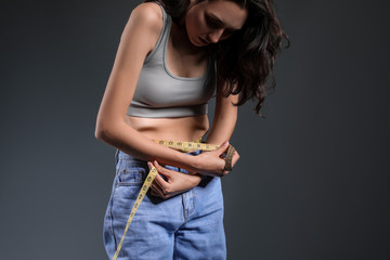 Sick woman measuring her waist on grey background. Concept of anorexia