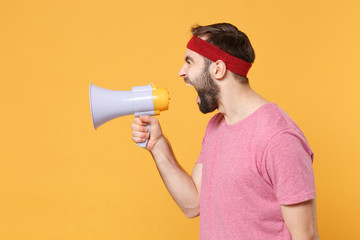 Side view of young bearded fitness sporty guy 20s sportsman in headband t-shirt spend weekend in home gym isolated on yellow wall background. Workout sport motivation concept. Screaming in megaphone.