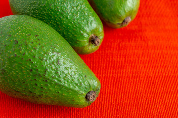 Aerial view of green avocados, with selective focus, on red tablecloth horizontally, with copy space