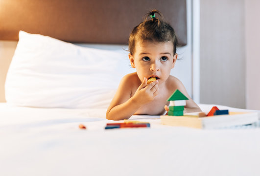 Horizontal image of cute baby girl playing with wood colorful toys in the bed. Toddler is playing with toy wooden at home. Child playing with colorful toy blocks in white bedroom. Educational game.