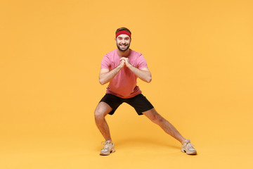 Fototapeta na wymiar Smiling fitness sporty guy sportsman in headband t-shirt spend weekend in home gym isolated on yellow background. Workout sport motivation concept. Doing squats lunges exercising holding hands folded.