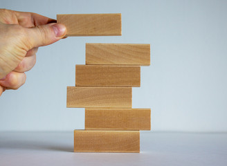 Concept of building success foundation. Men hand put wooden blocks on the stack of wooden blocks.
