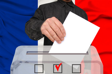male voter drops a ballot in a transparent ballot box against the background of the national flag...