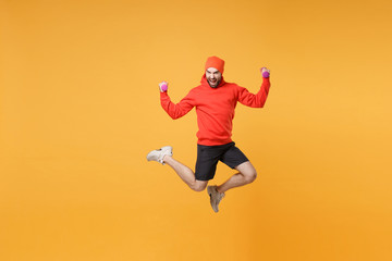 Fototapeta na wymiar Screaming bearded fitness sporty guy sportsman in hat, hoodie, shorts spend weekend in home gym isolated on yellow background. Workout sport motivation concept. Jumping doing exercise with dumbbell.