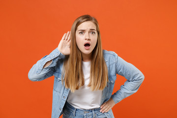Shocked young woman girl in casual denim clothes posing isolated on orange wall background studio...