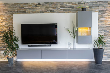 Modern and cozy interior of a living room in a luxury appartement, big window and tv with stone wall