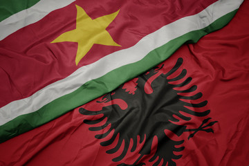 waving colorful flag of albania and national flag of suriname.