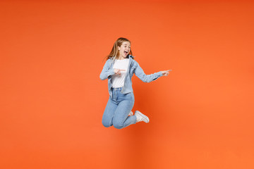 Fototapeta na wymiar Excited young woman girl in casual denim clothes posing isolated on orange background studio portrait. People lifestyle concept. Mock up copy space. Having fun pointing index fingers aside jumping.