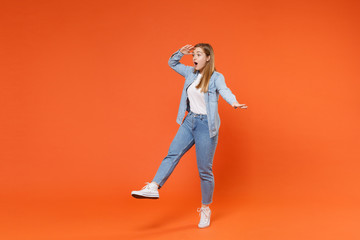 Shocked young woman girl in casual denim clothes posing isolated on orange background studio portrait. People lifestyle concept. Mock up copy space. Holding hand at forehead looking far away distance.