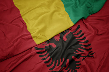 waving colorful flag of albania and national flag of guinea.