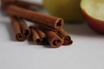 several sticks of cinnamon lie on top of each other close up next to apples red green yellow on a white background with a place to insert text or product product