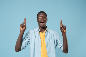 Fototapeta premium Shocked young african american man guy in casual shirt, yellow t-shirt posing isolated on blue wall background studio portrait. People lifestyle concept. Mock up copy space. Pointing index fingers up.
