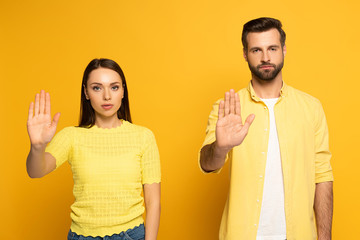 Young couple showing stop gesture at camera on yellow background