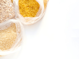 dry goods in cellophane bags, stockpiling, donation, delivery, volunteer, food supplies for staying home concept. Vermicelli, oatmeal, rice on white background, copyspace