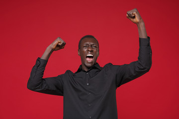 Screaming young african american man guy in classic black shirt posing isolated on red background...