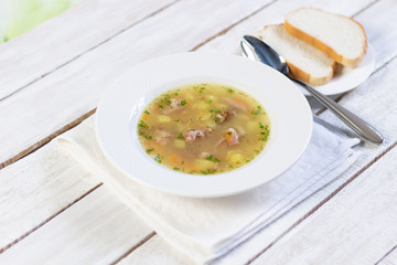 Pea soup with smoked meat and potato in white plate on table cloth with spoon and bread on wooden background