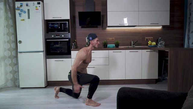The athlete performs lunges in a jump with a change of legs in home isolation. A man trains the quadriceps, gluteus, abdominal muscles.