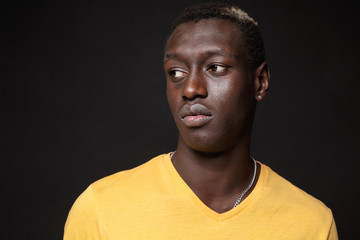 Close up of young african american man guy in yellow t-shirt posing isolated on black wall background studio portrait. People sincere emotions lifestyle concept. Mock up copy space. Looking aside.