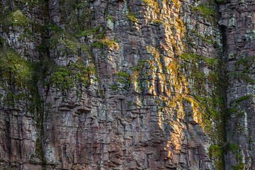 Impressive details of layers of a textured, vertical, rocky cliff covered by colorful moss and grass, lighten by soft sunlight in canyon in Serbia called Small Colorado