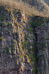 Impressive details of layers of a textured, vertical, rocky cliff covered by colorful moss and grass, lighten by soft sunlight in canyon in Serbia called Small Colorado