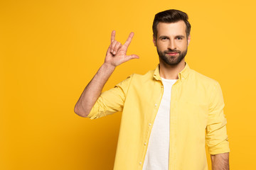 Handsome man showing word love in sign language on yellow background
