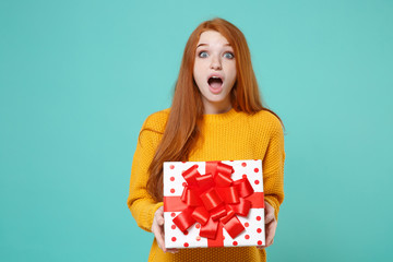 Shocked redhead girl in yellow sweater posing isolated on blue turquoise background. Valentine's...