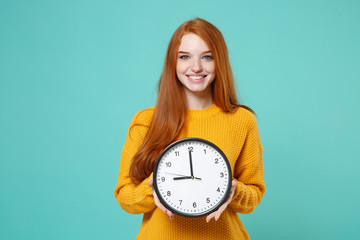 Smiling young redhead woman girl in yellow knitted sweater posing isolated on blue turquoise wall...
