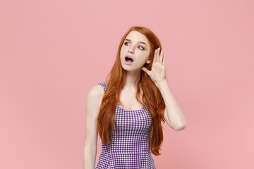 Curious young redhead woman girl in plaid dress posing isolated on pastel pink background studio...