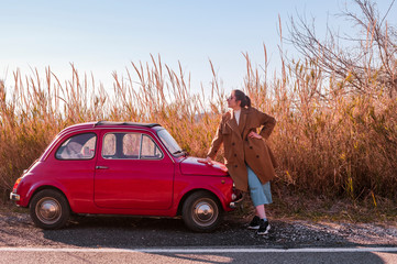 Beautiful lady standing near retro car. Young girl posing near a red car on a background of sunset...