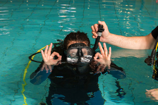 Instructor Assisting Woman In Scuba Diving In Swimming Pool