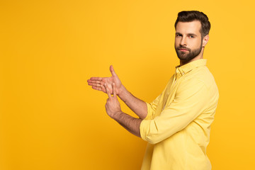 Side view of young man showing sign in deaf and dumb language on yellow background