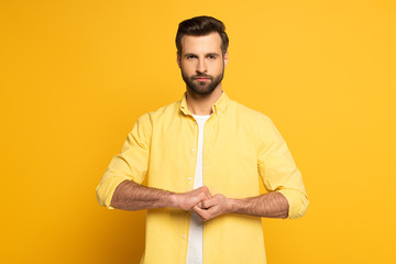 Handsome man showing cohesion sign in deaf and dumb language on yellow background © LIGHTFIELD STUDIOS