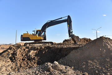 Excavator working at construction site on earthworks. Backhoe digs ground for the foundation and for paving out sewer line. Construction machinery for excavating, loading, lifting and hauling of cargo