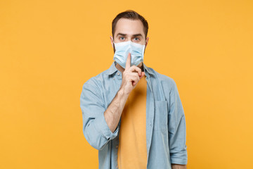 Secret young man in sterile face mask posing isolated on yellow background. Epidemic pandemic...