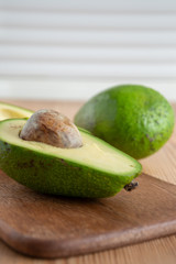 Top view of half avocado and one whole one, with selective focus, on wooden board and white background, vertical